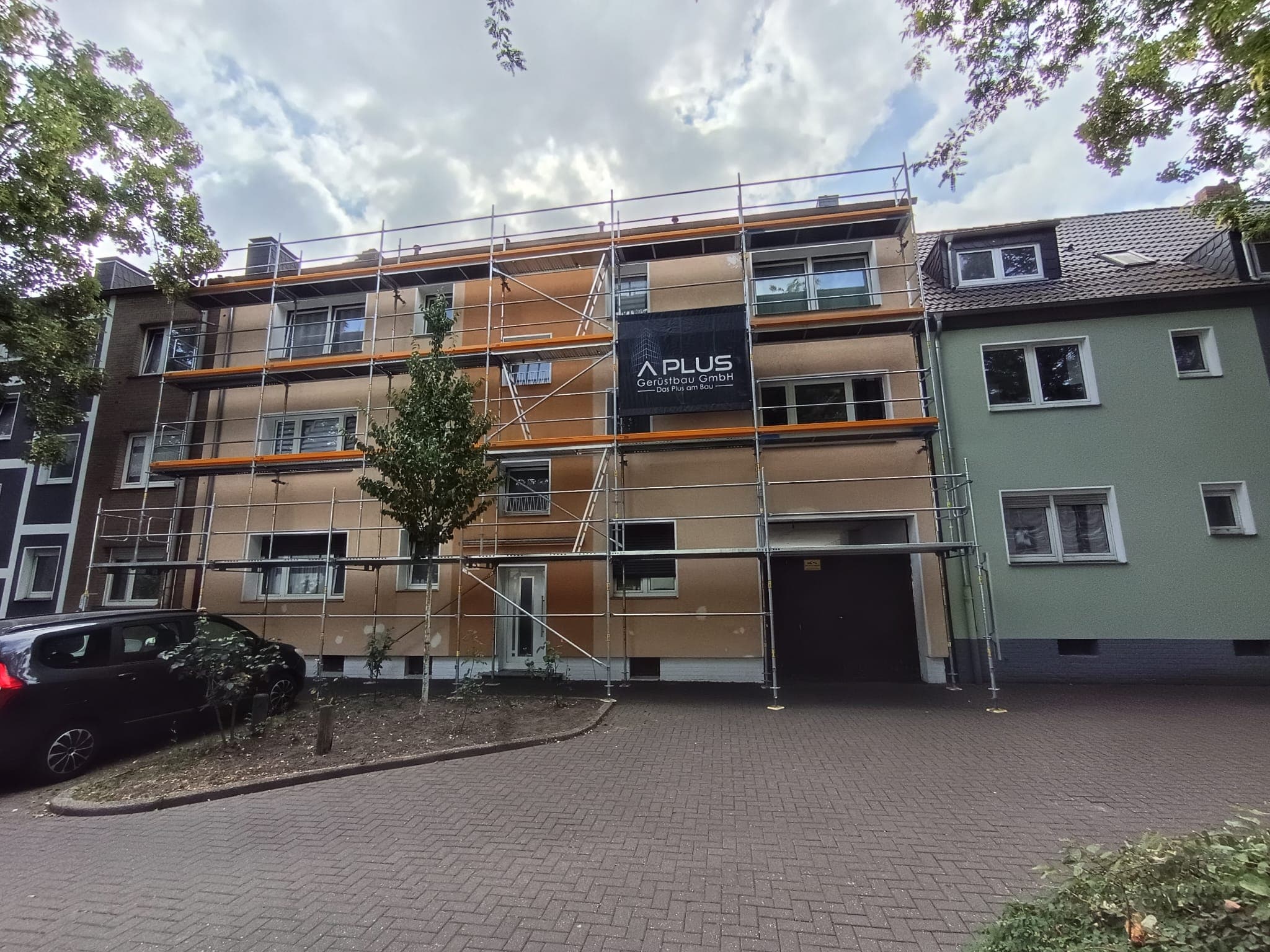 Eingerüstetes Mehrfamilienhaus mit Banner der A PLUS Gerüstbau
